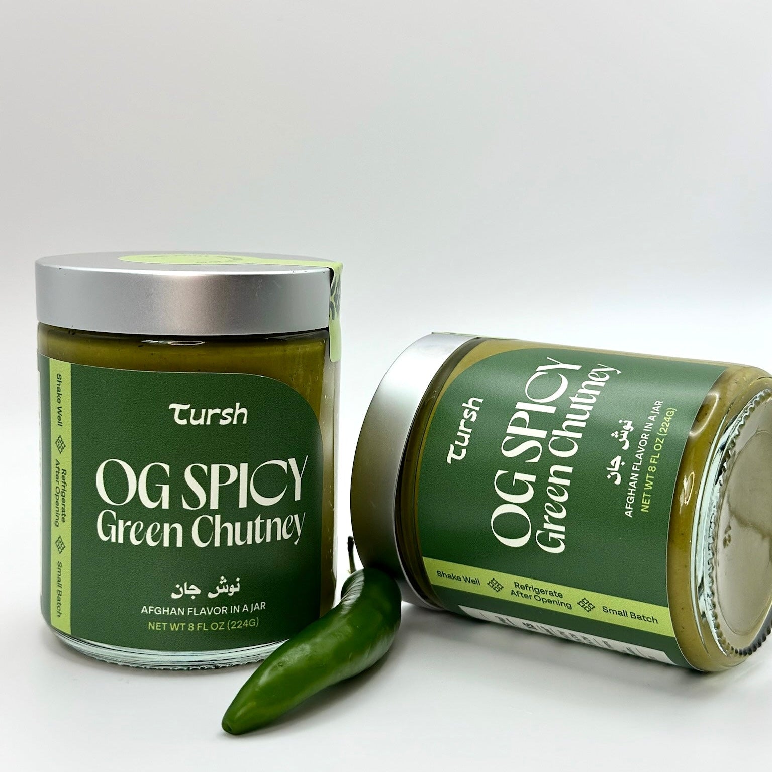 two 8 oz jar of green chutney with white background and one green serrano pepper